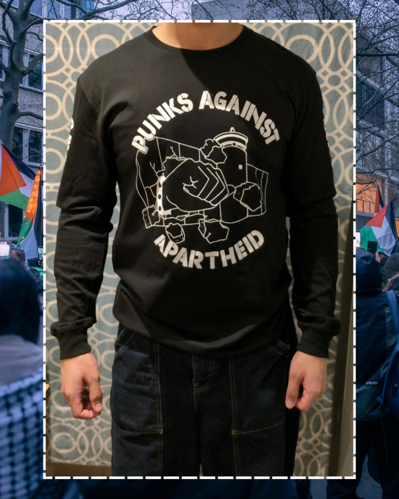 A photo of an individual facing forwards from the neck downards, showing the PAA logo (a fist with a spikey bracelet punching through the apartheid wall).